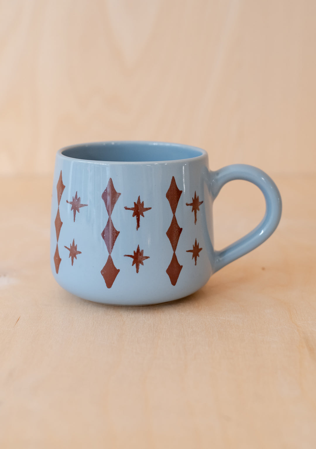 Hand-painted TBCo Celestial Blue Mug featuring brown diamond and star pattern on light blue ceramic, with curved handle