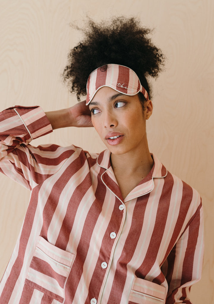 TBCo Cotton Eye Mask in red and white stripes shown with matching striped pyjamas against beige background