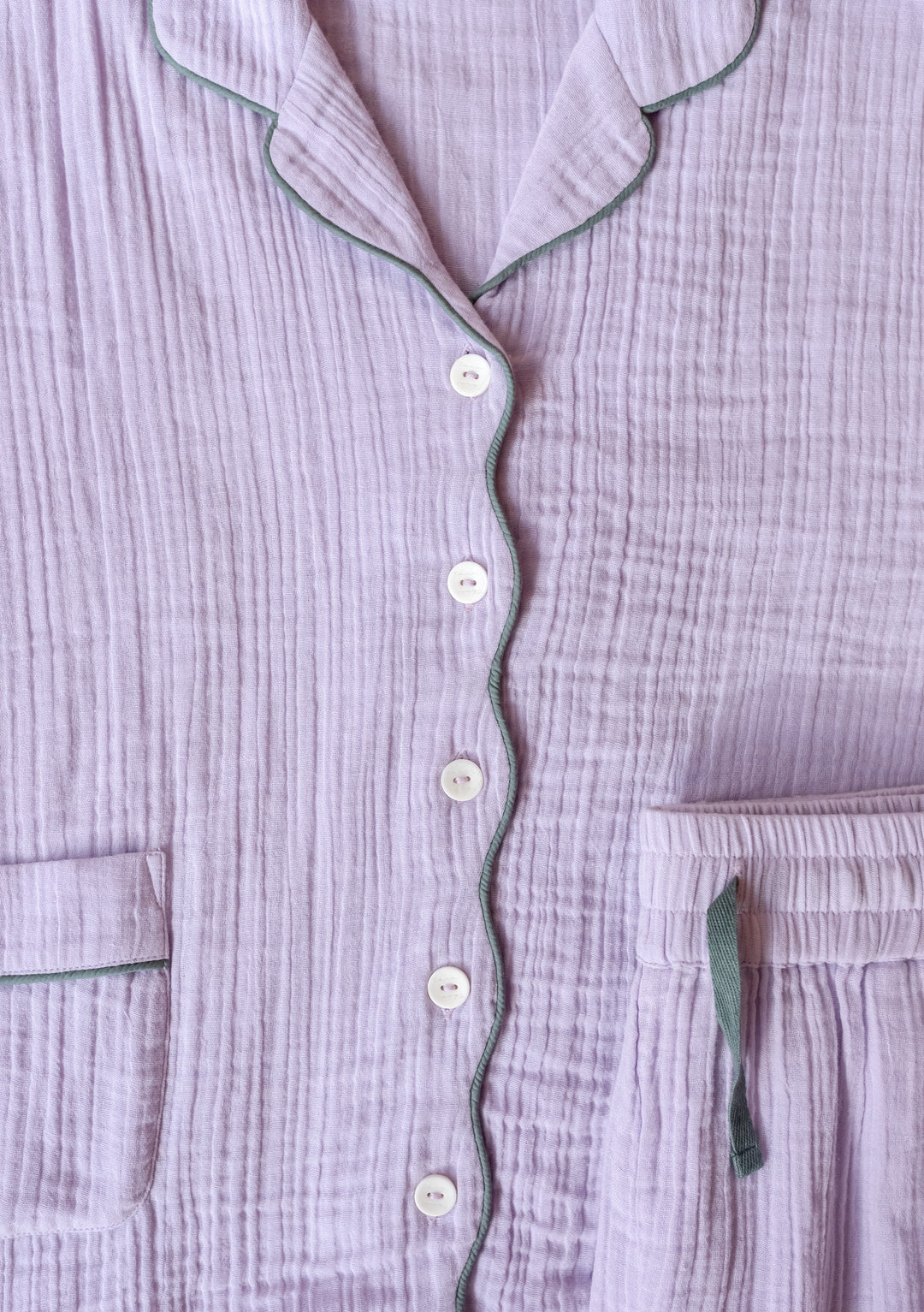 Close-up of TBCo Cotton Pyjamas in Lilac featuring crinkle gauze fabric, sage piping trim, white buttons and patch pockets