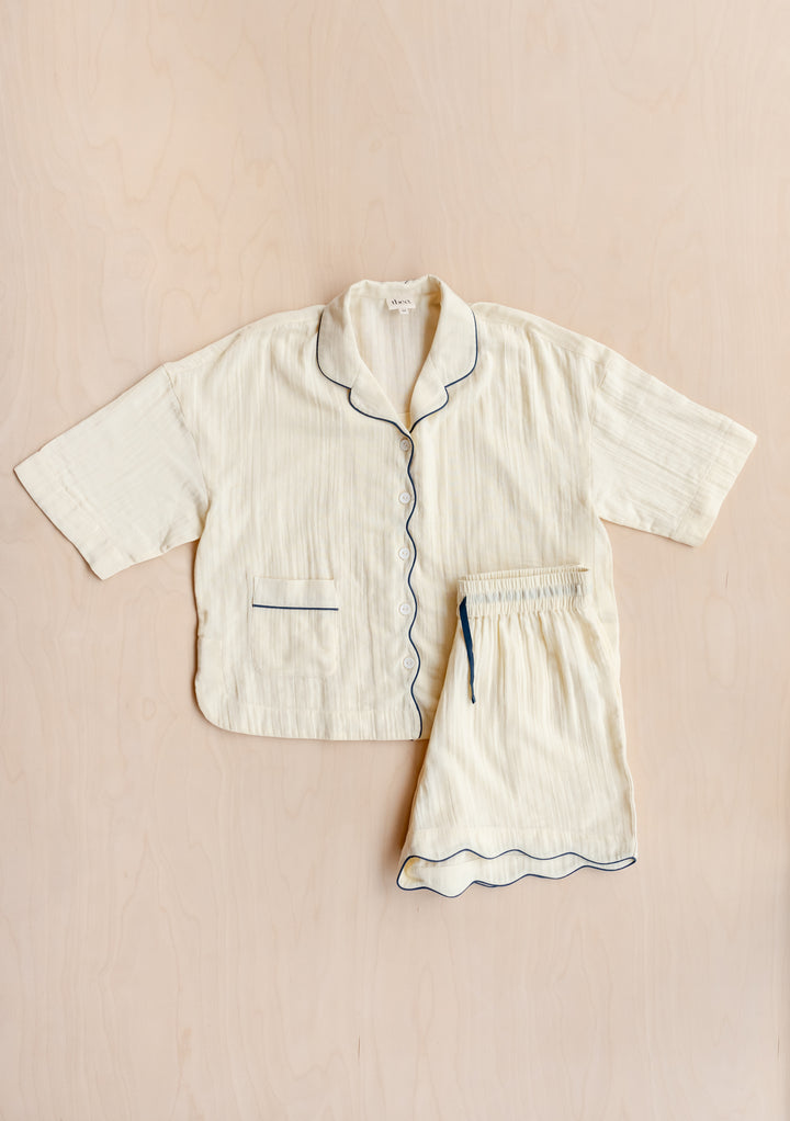 TBCo Cotton Pyjamas in Buttermilk with navy piping, featuring scalloped edges and squiggle embroidery, laid flat on beige surface