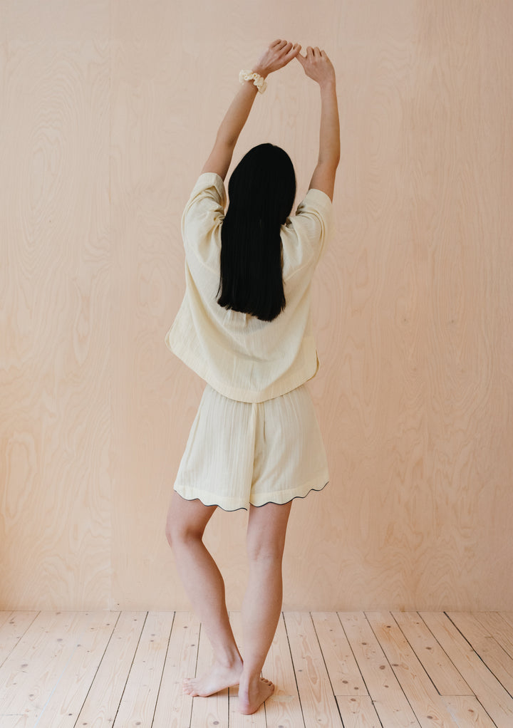 Person stretching in TBCo buttermilk cotton pyjamas with scalloped shorts and boxy top against pink wall