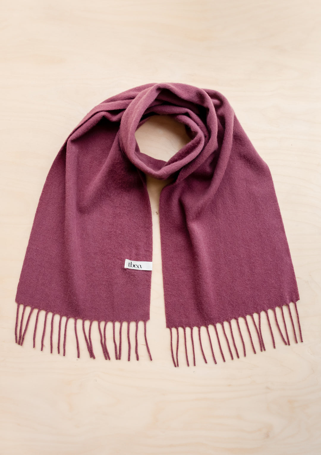 Soft mulberry-coloured TBCo lambswool scarf with fringed ends displayed on neutral background, showcasing luxurious texture