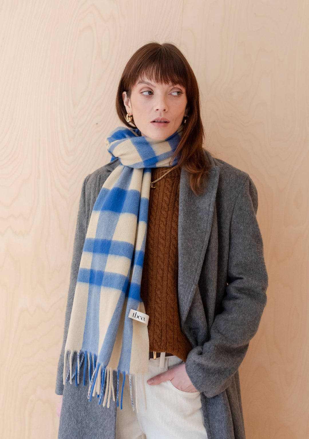 TBCo Lambswool Oversized Scarf in blue and cream check pattern, styled with grey coat and brown jumper, showing fringe detail