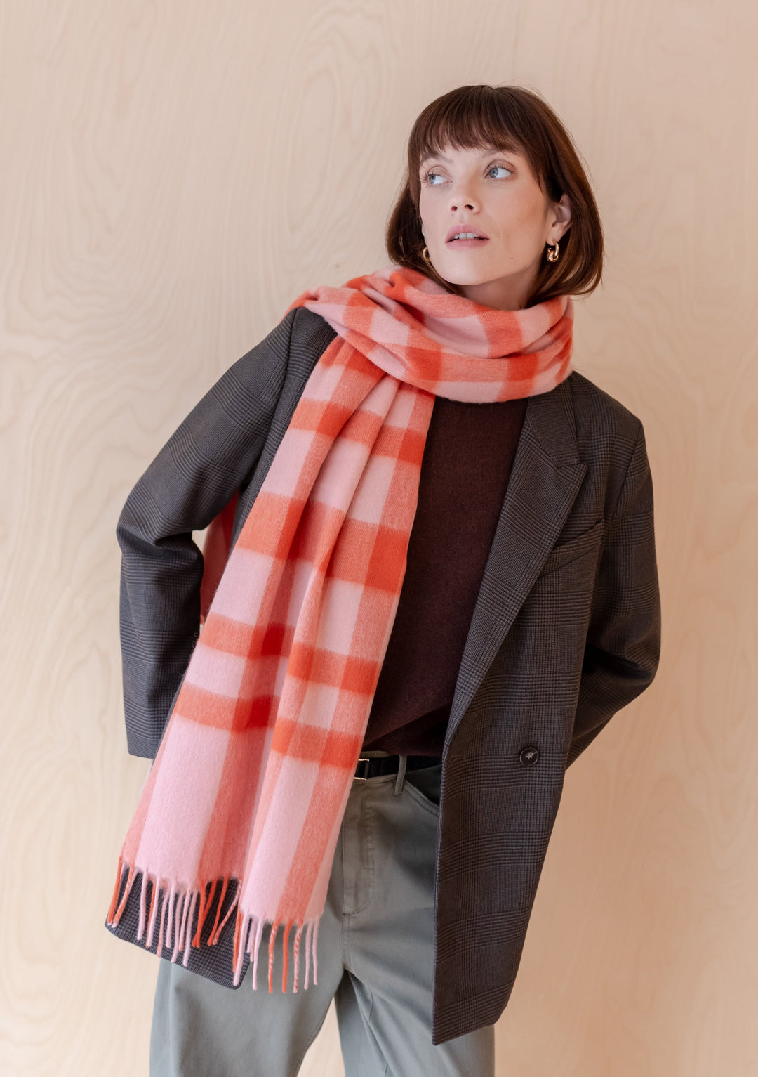 Pink and red check pattern TBCo lambswool oversized scarf styled with grey blazer and trousers against neutral background