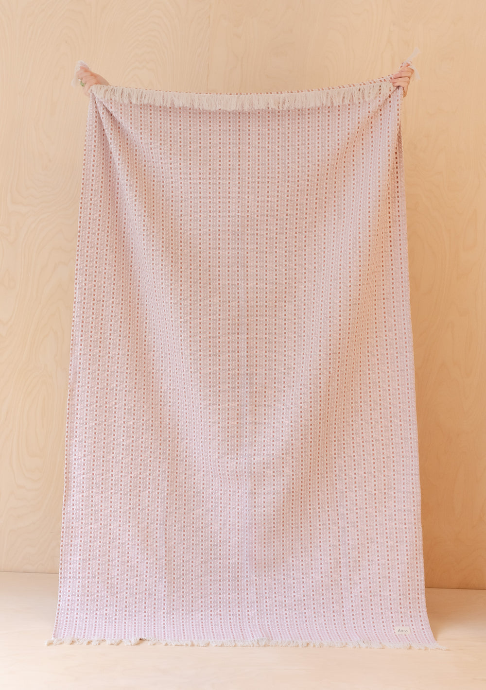 TBCo Cotton Throw in Pink Geometric displayed vertically, showing textured dotted pattern and tasselled edges on beige background