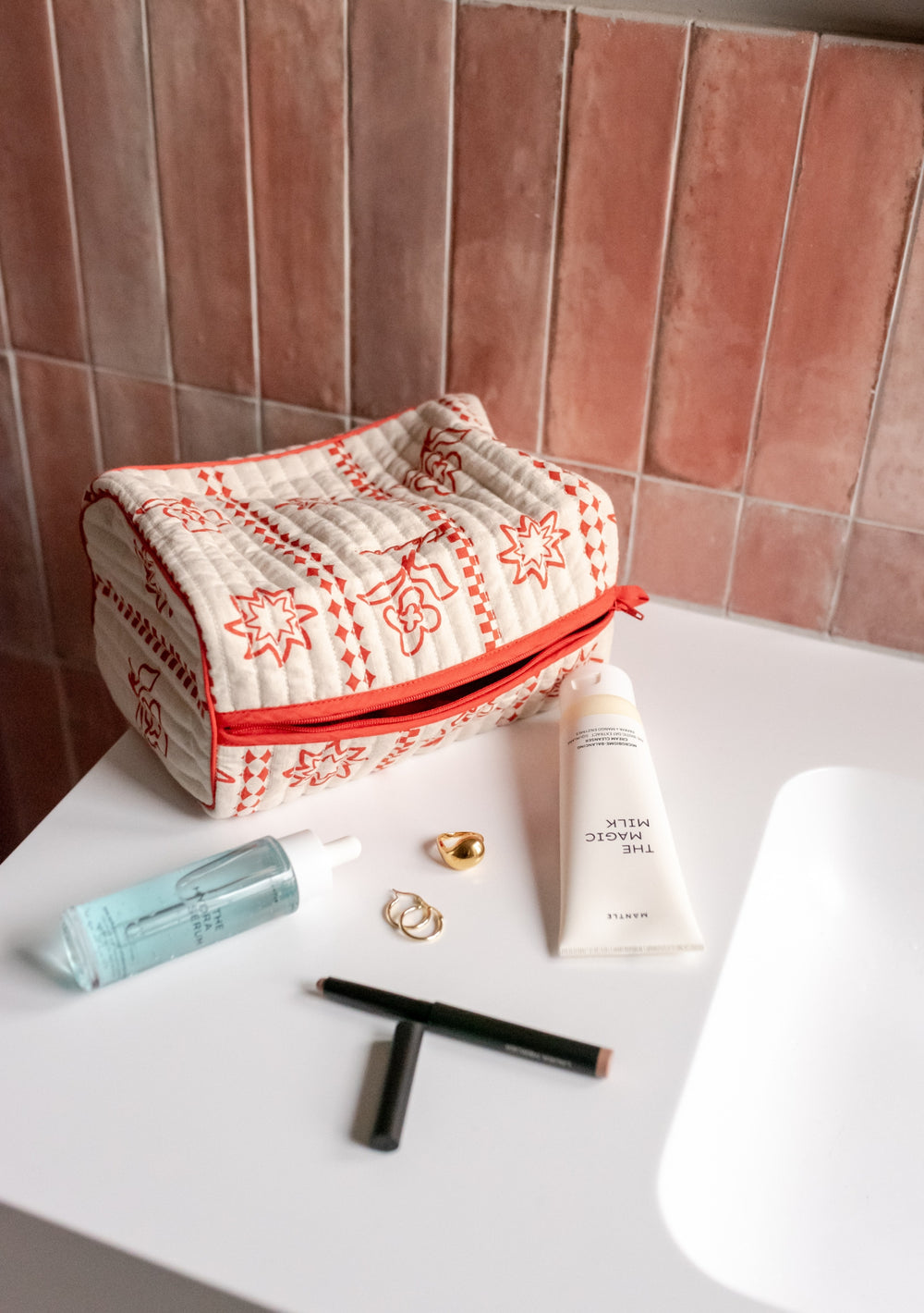 TBCo Cotton Wash Bag in Flora featuring red floral pattern and zip closure, displayed with toiletries on white surface against terracotta tiles